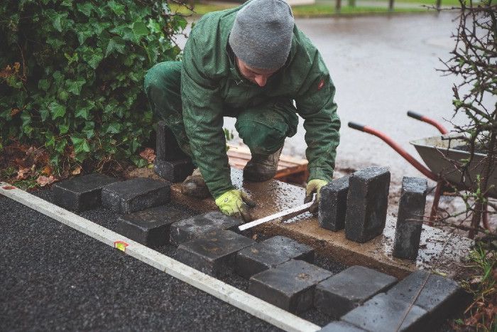 Ein Handwerker legt die ersten Pflastersteine für einen Gartenweg.